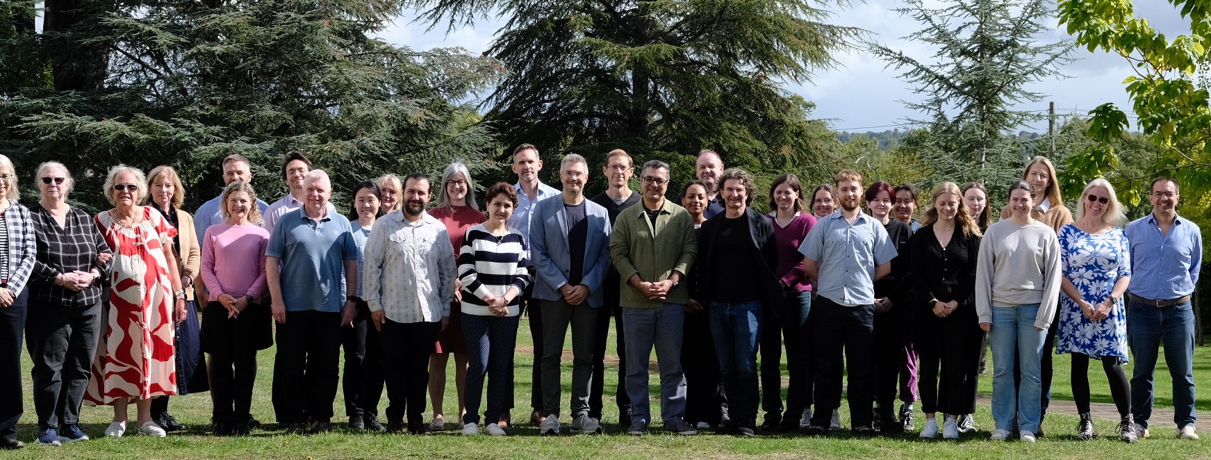 A group of people standing in a line in front of trees in the sunshine.